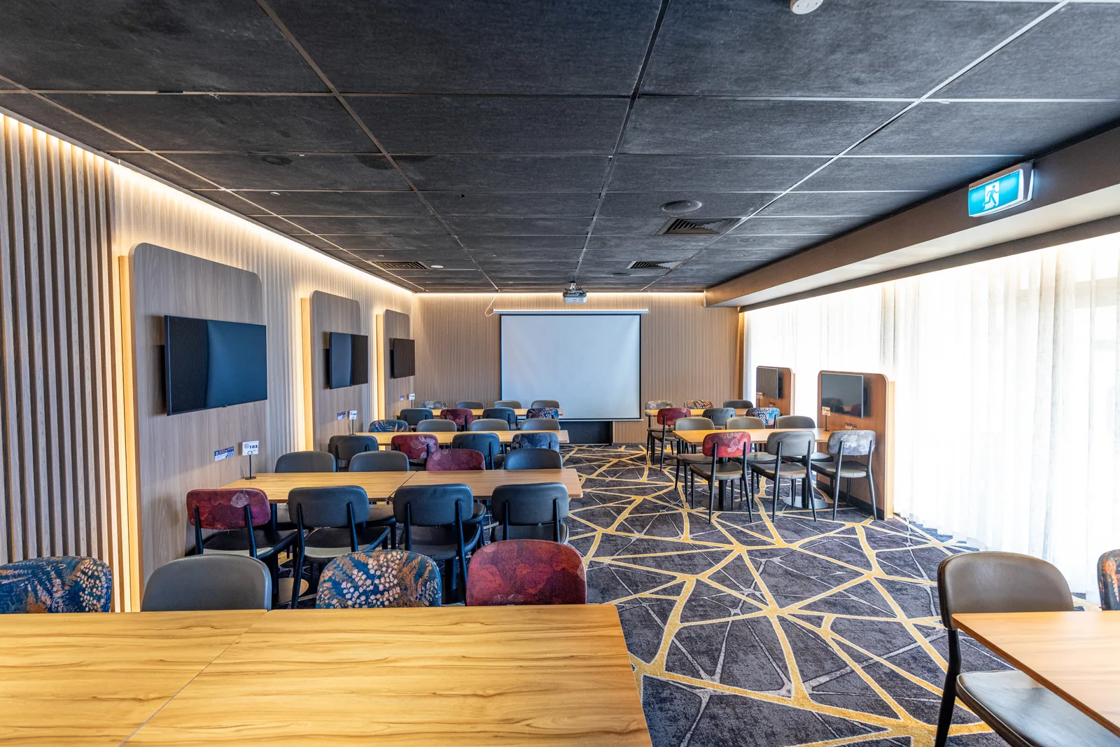 The restaurant set with long tables and chairs facing the projector screen, wall screens down one side