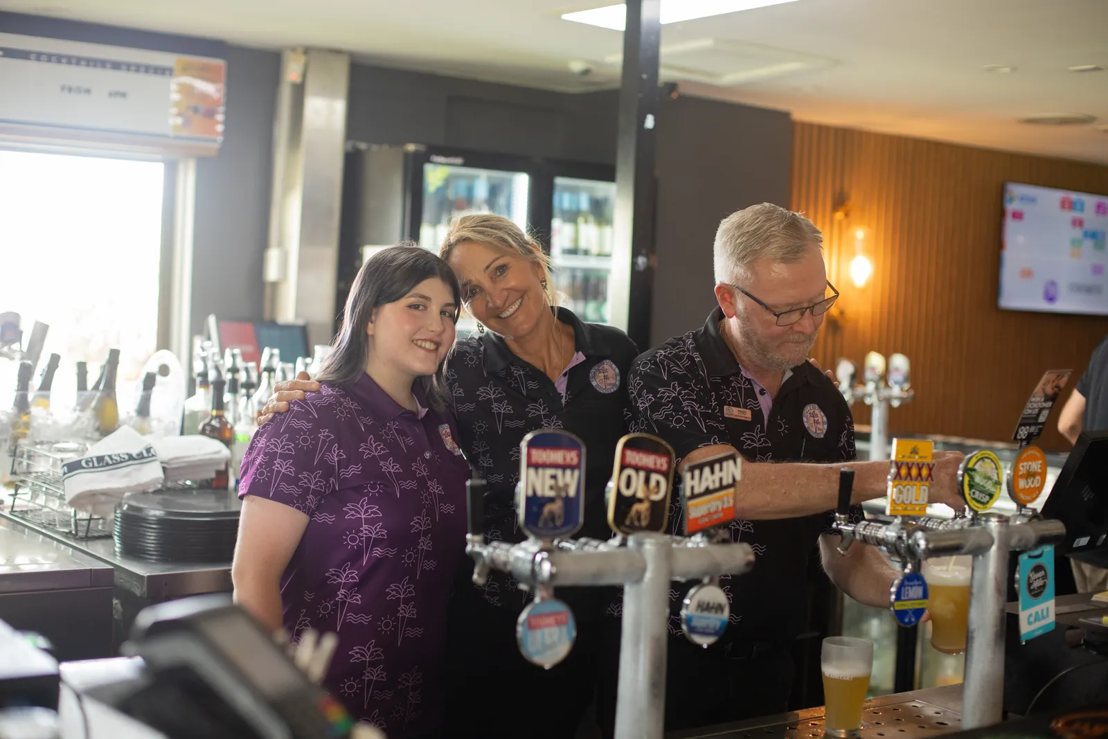 Three Pottsville Sports bar staff smiling together behind the taps while pouring a beer